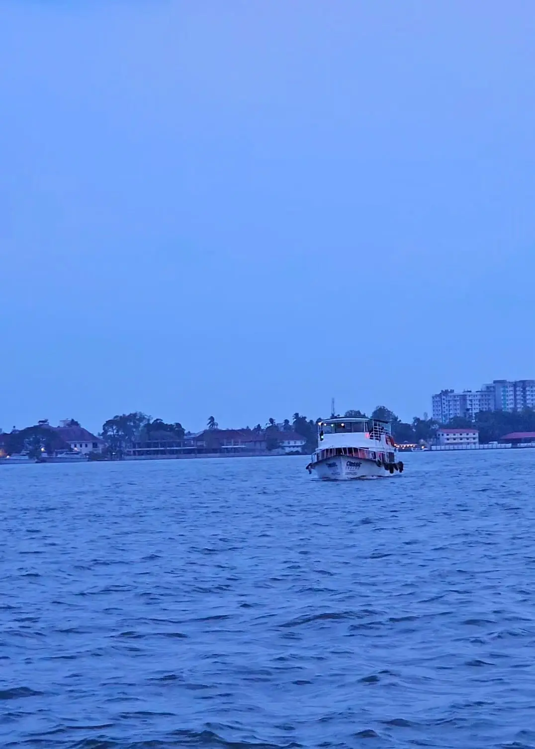 One of the best digital marketer in Thrissur captured A boat moving across calm water at dusk with city buildings and trees visible along the shoreline
