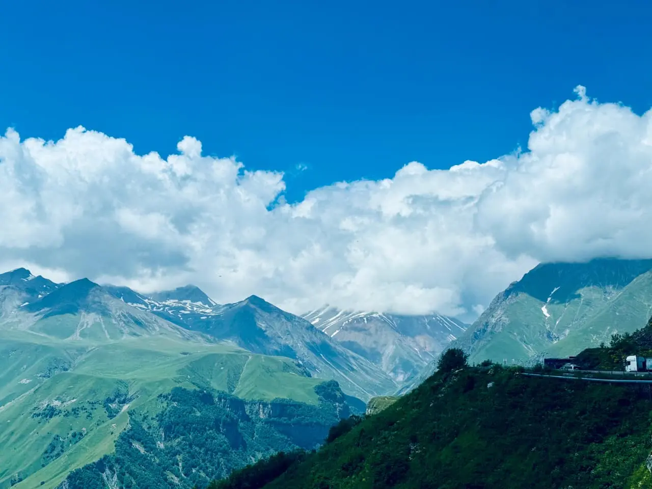 one of the best digital marketer in Thrissure captured "Lush green mountain landscape with rolling hills, dramatic clouds, and a winding road under a bright blue sky.