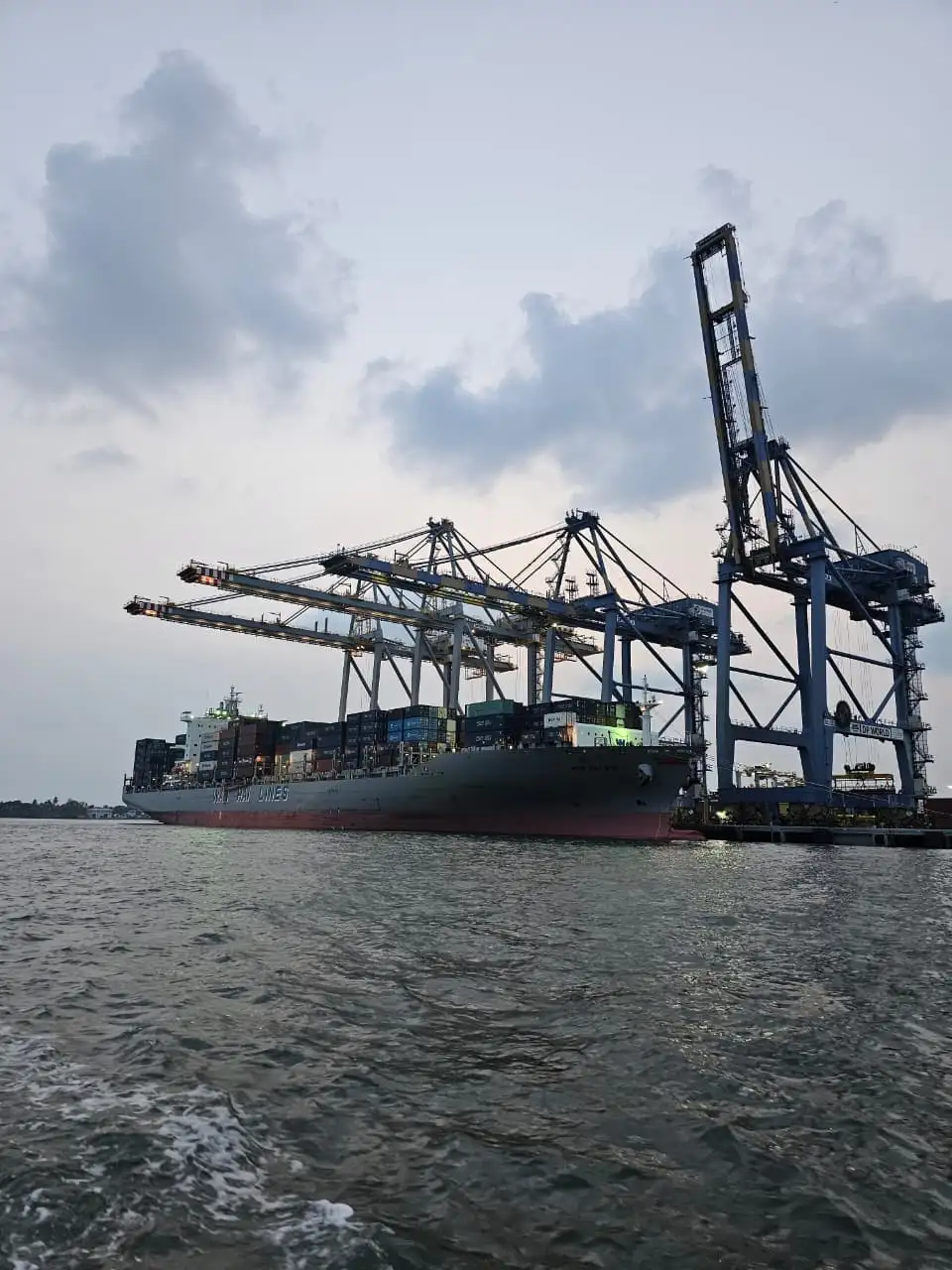one of the best digital marketer in thrissur caotured “Large container ship docked at a port with cargo cranes overhead, floating on calm water under daylight."